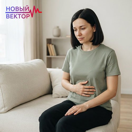 Женщина сидит на диване, придерживая область живота рукой из-за недомогания, которое может потребовать исключения печеночной недостаточности перед кодированием Налтрексоном